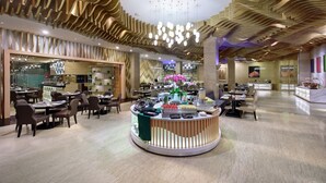A spacious hotel lobby with a central reception desk, multiple dining areas, and a modern ceiling design. - JS Luwansa Hotel and Convention Center (Jakarta)