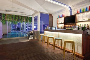 A rooftop bar with a pool, bar stools, and a menu board.