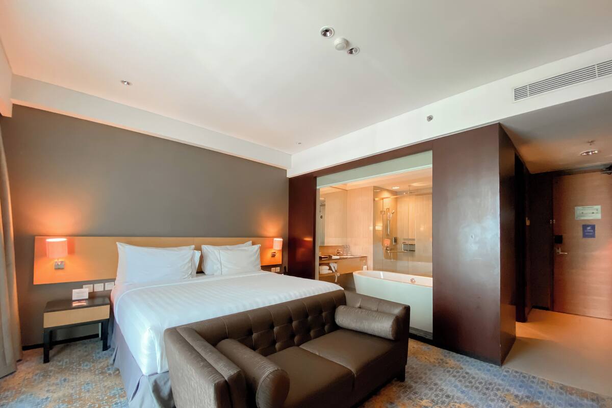 A hotel room with a large bed, a sitting area, a bathroom with a bathtub, and a mirror.