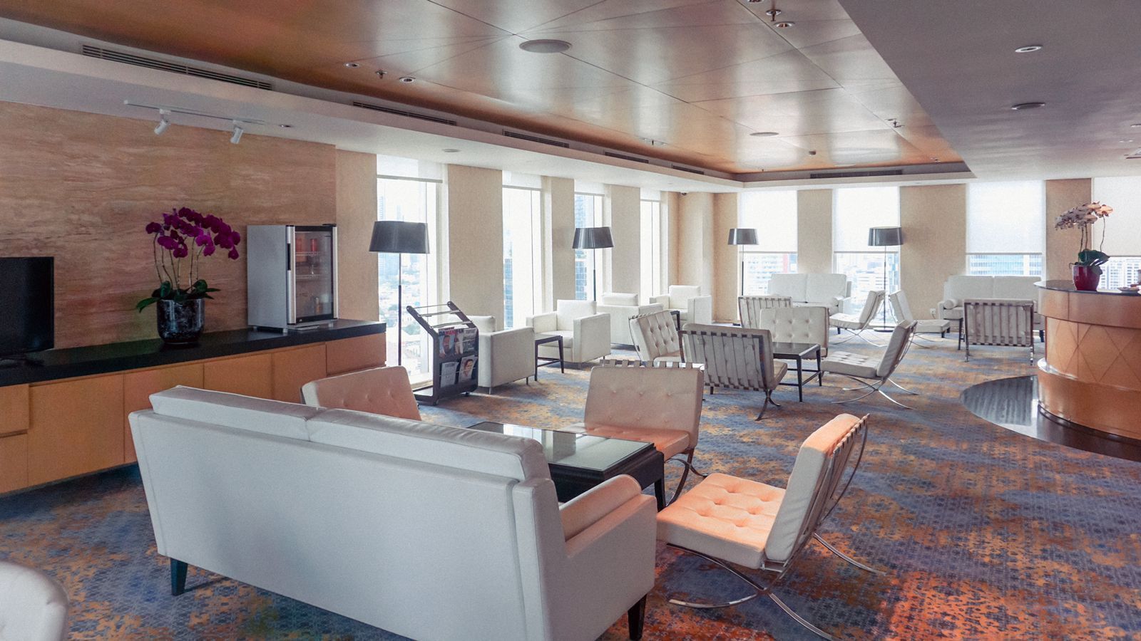 A spacious lobby with a modern design, featuring a mix of seating areas, a reception desk, and large windows providing natural light.