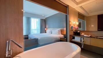 Una habitación de hotel moderna con una bañera grande, una cama bien hecha, un tocador con espejo y vistas a la ciudad desde la ventana.