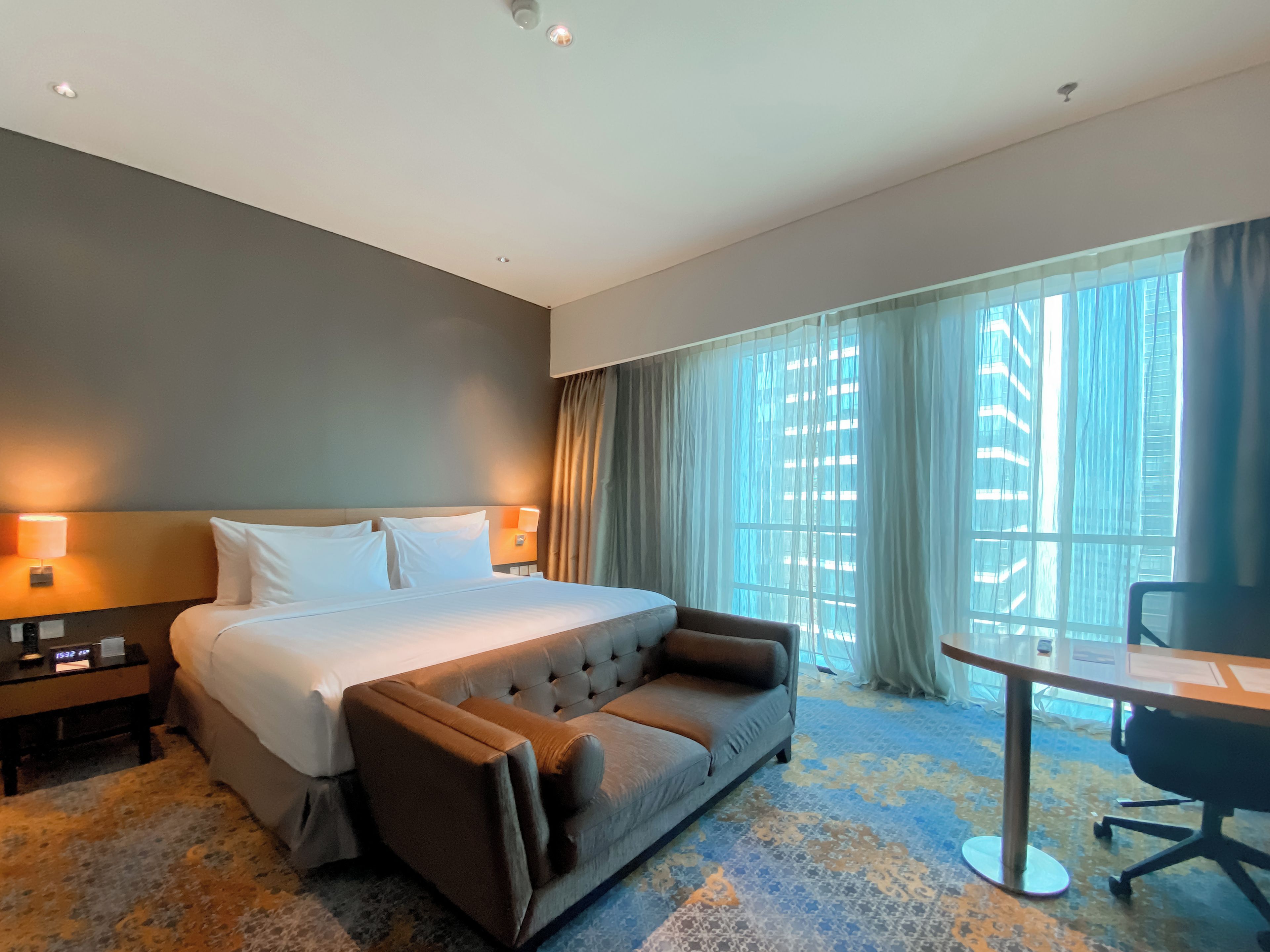 A hotel room with a bed, a sofa, a desk, and a window with curtains.