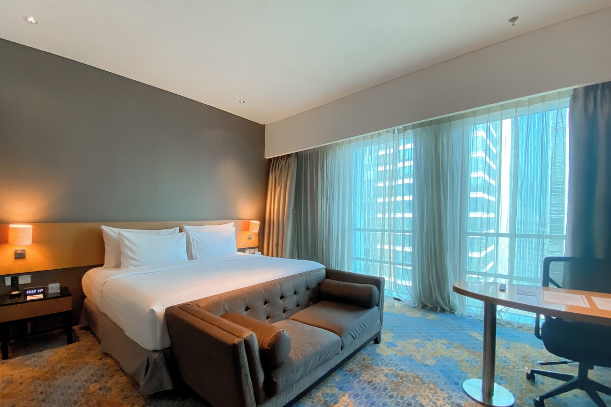 A hotel room with a bed, a sofa, a desk, and a window with curtains.