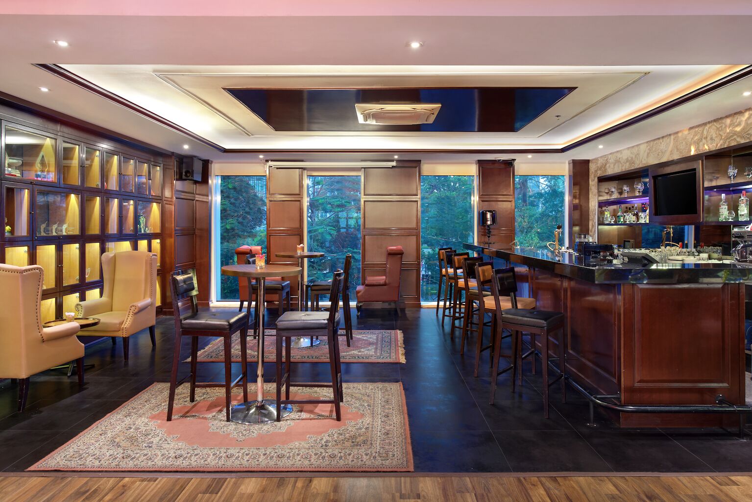 A modern bar area with a bar counter, seating, and a view of the outdoors.