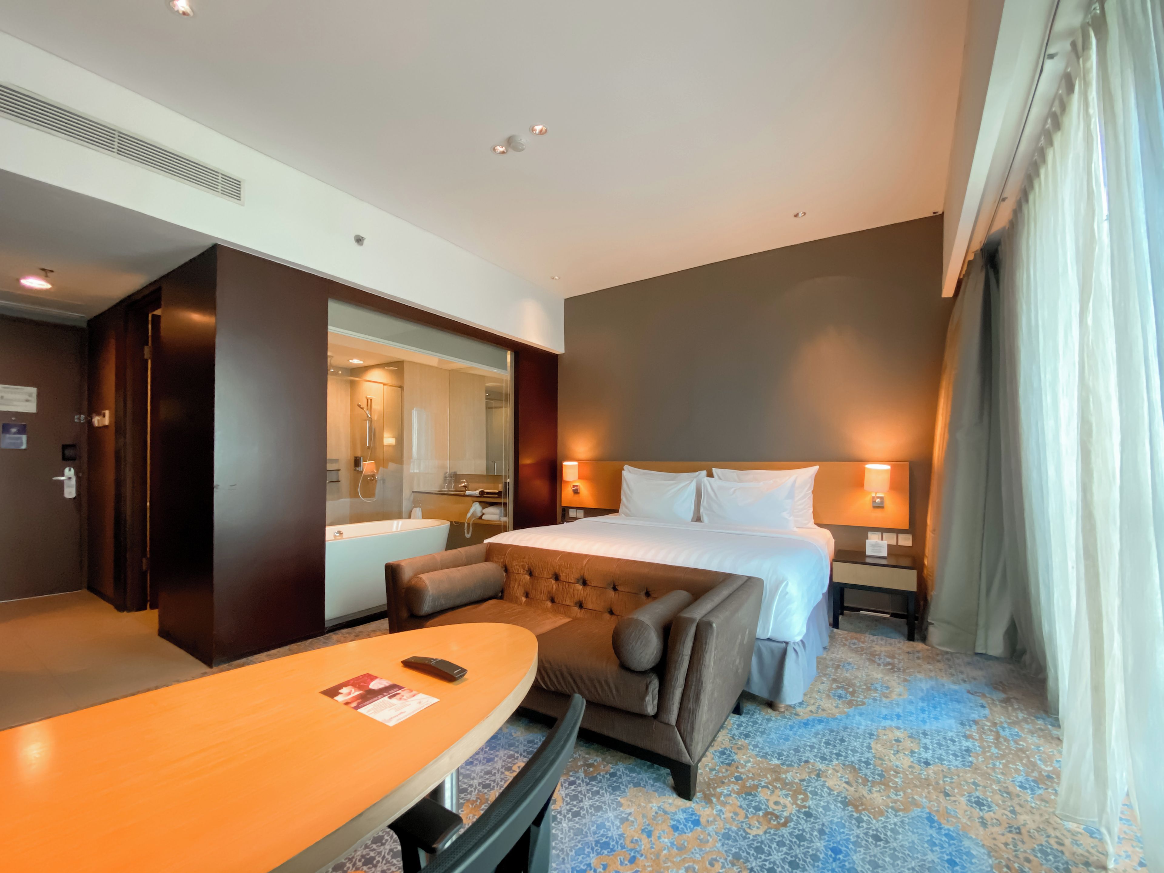A hotel room with a bed, bedside tables, a desk, a chair, a bathroom with a bathtub, and a large mirror.