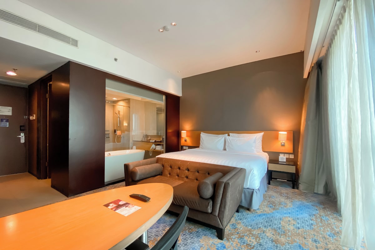A hotel room with a large bed, a seating area with a table, a bathroom with a bathtub, and a large mirror.