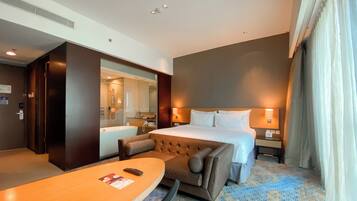A hotel room with a bed, bedside tables, a desk, a chair, a bathroom with a bathtub, and a large mirror.