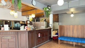 Un comptoir d’accueil avec un comptoir en bois, une horloge et un coffre-fort. On y trouve également un banc bleu et un ventilateur au plafond.