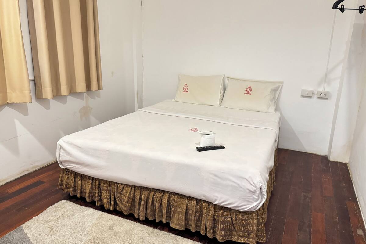 Een net opgemaakt bed met een witte spreideken en een bedrok met een patroon.