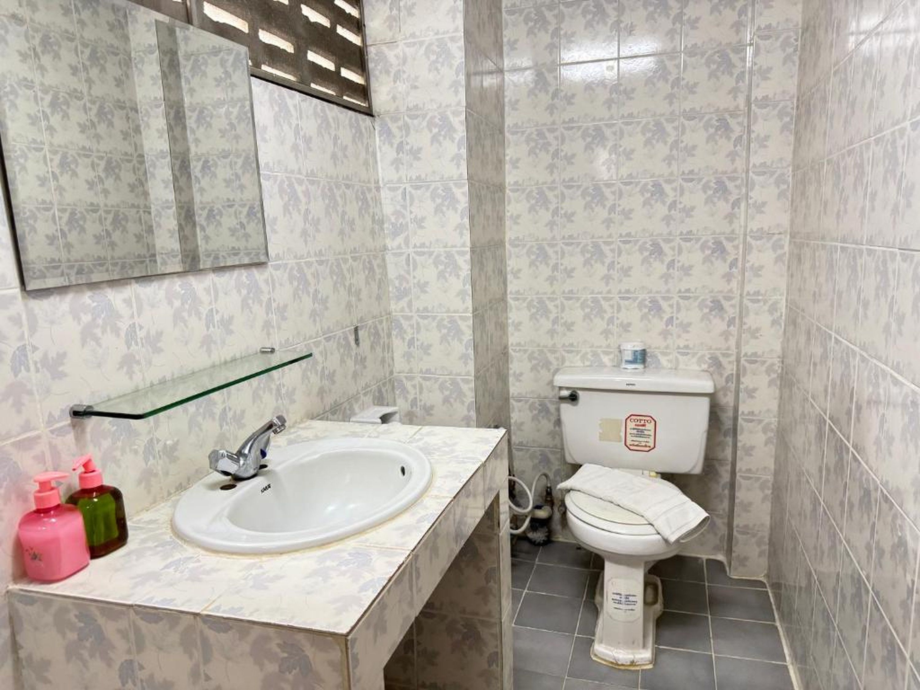 A bathroom with a white sink, a glass shelf, a toilet, and a mirror.