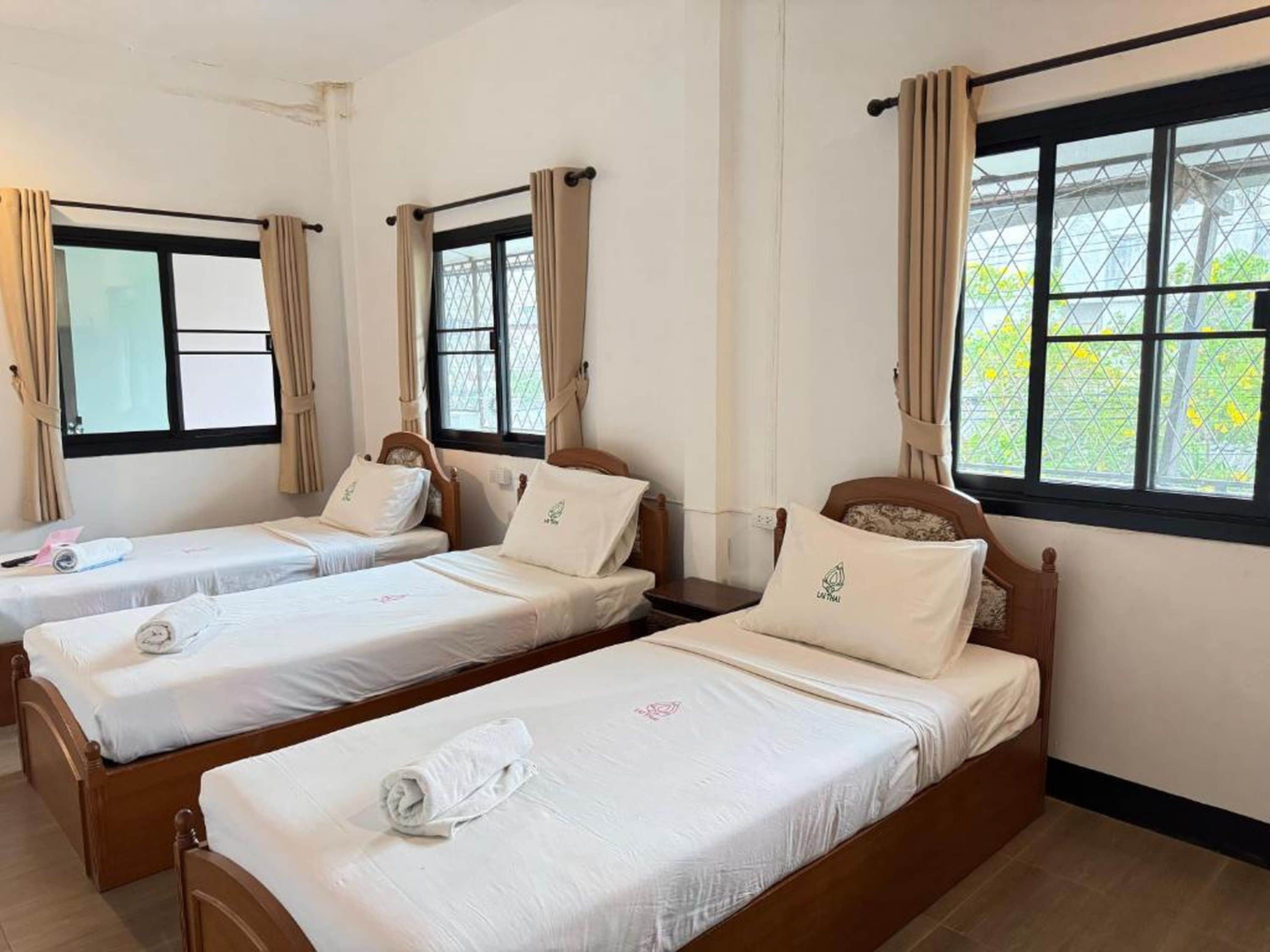 A hotel room with three single beds, each with a pillow and a rolled towel.