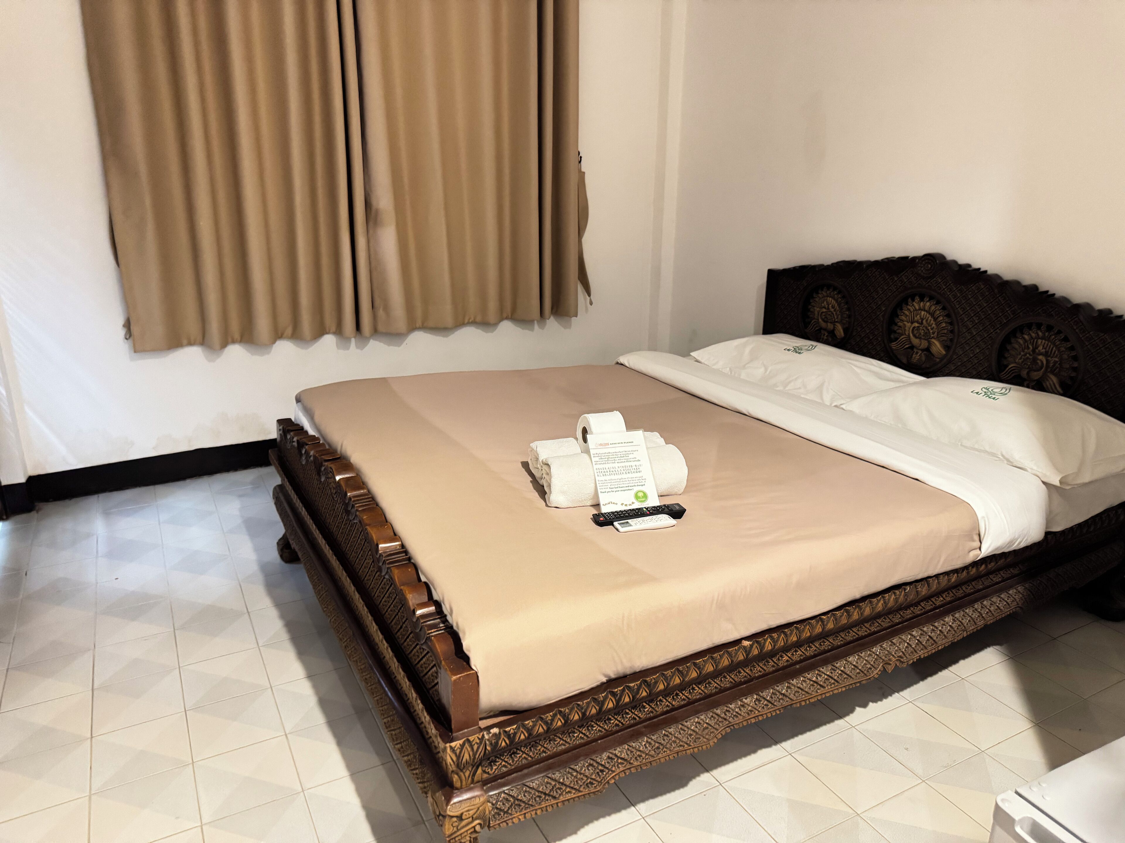A neatly made bed with a beige bedspread, a pillow with a logo, and a remote control on the bed.