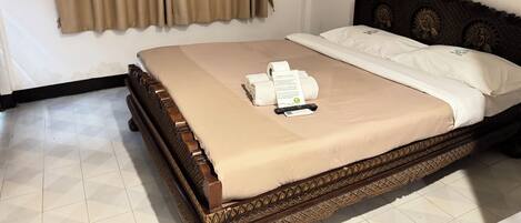 A neatly made bed with a beige bedspread, a pillow with a logo, and a remote control on the bed.