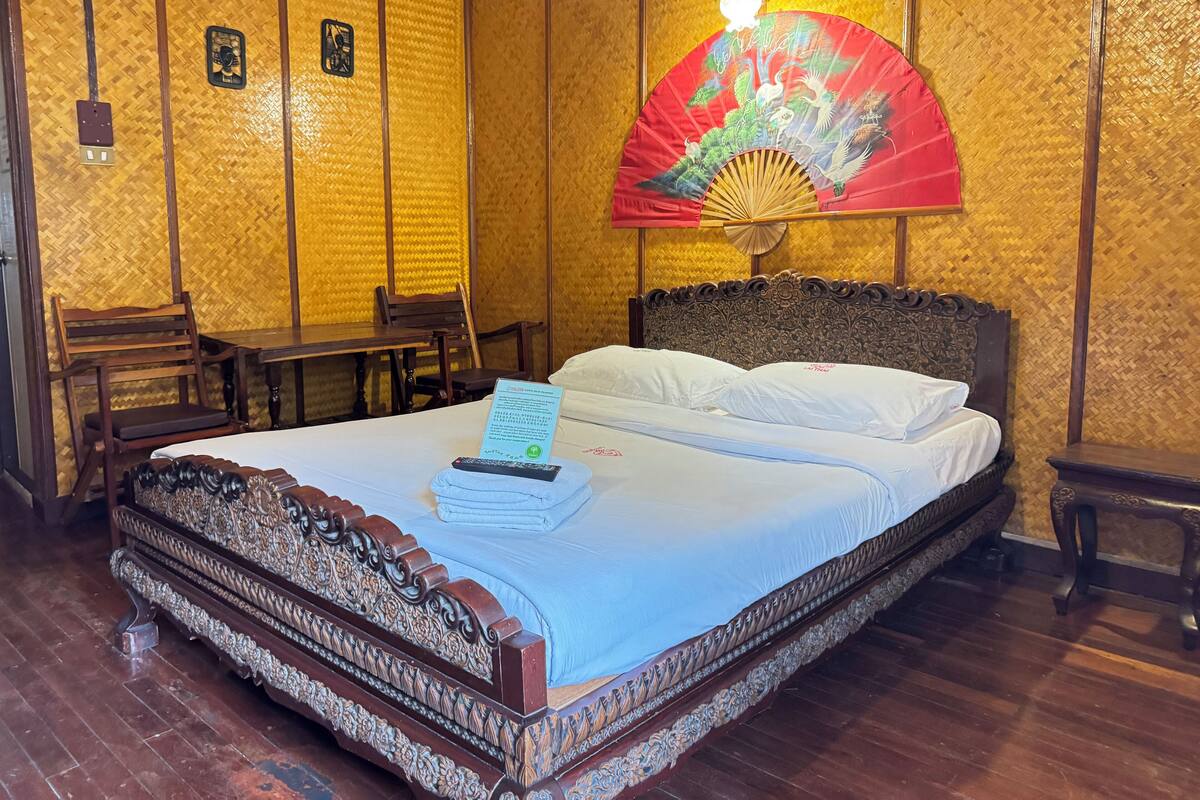 Een klassieke kamer met een bed, houten meubels, een ventilator en een wand met geweven patroon.