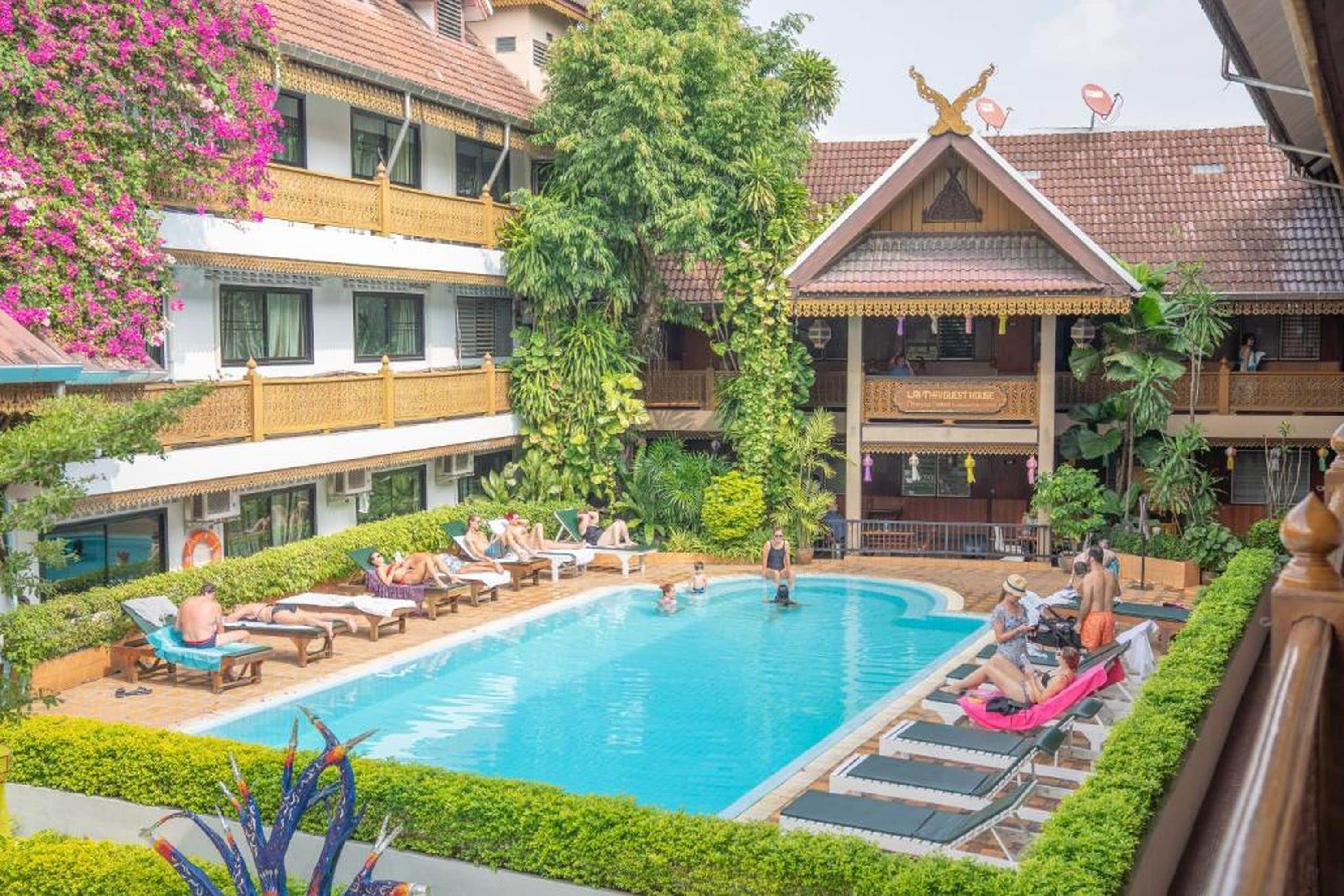 A hotel with a swimming pool surrounded by lounge chairs and greenery.