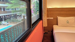Une chambre d’hôtel avec un lit, une fenêtre donnant sur une cour et une tête de lit en bois.