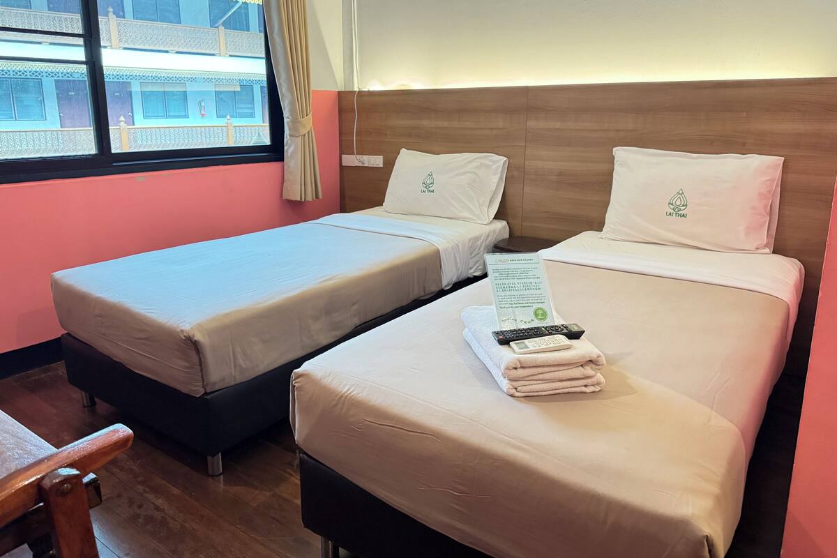 Een hotelkamer met twee bedden, een houten vloer, een raam met uitzicht op gebouwen en een bordje op het bed.