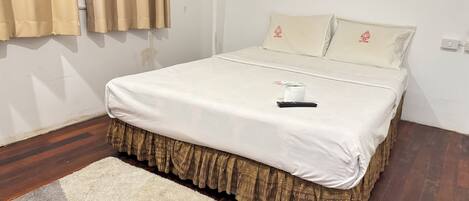 Una cama bien hecha con una colcha blanca y una falda estampada, un control remoto y una toalla enrollada sobre la cama.