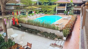 Une piscine avec des chaises longues, un espace repas avec une table et des chaises, et un bâtiment doté d’un toit traditionnel en arrière-plan.