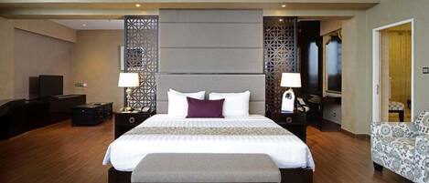 Ein modernes Hotelzimmer mit einem großen Bett, Nachttischen, einem Fernseher und einem gemusterten Sofa.