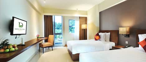 A hotel room with two beds, a desk with a fruit bowl, a TV, and a view of the outdoors.