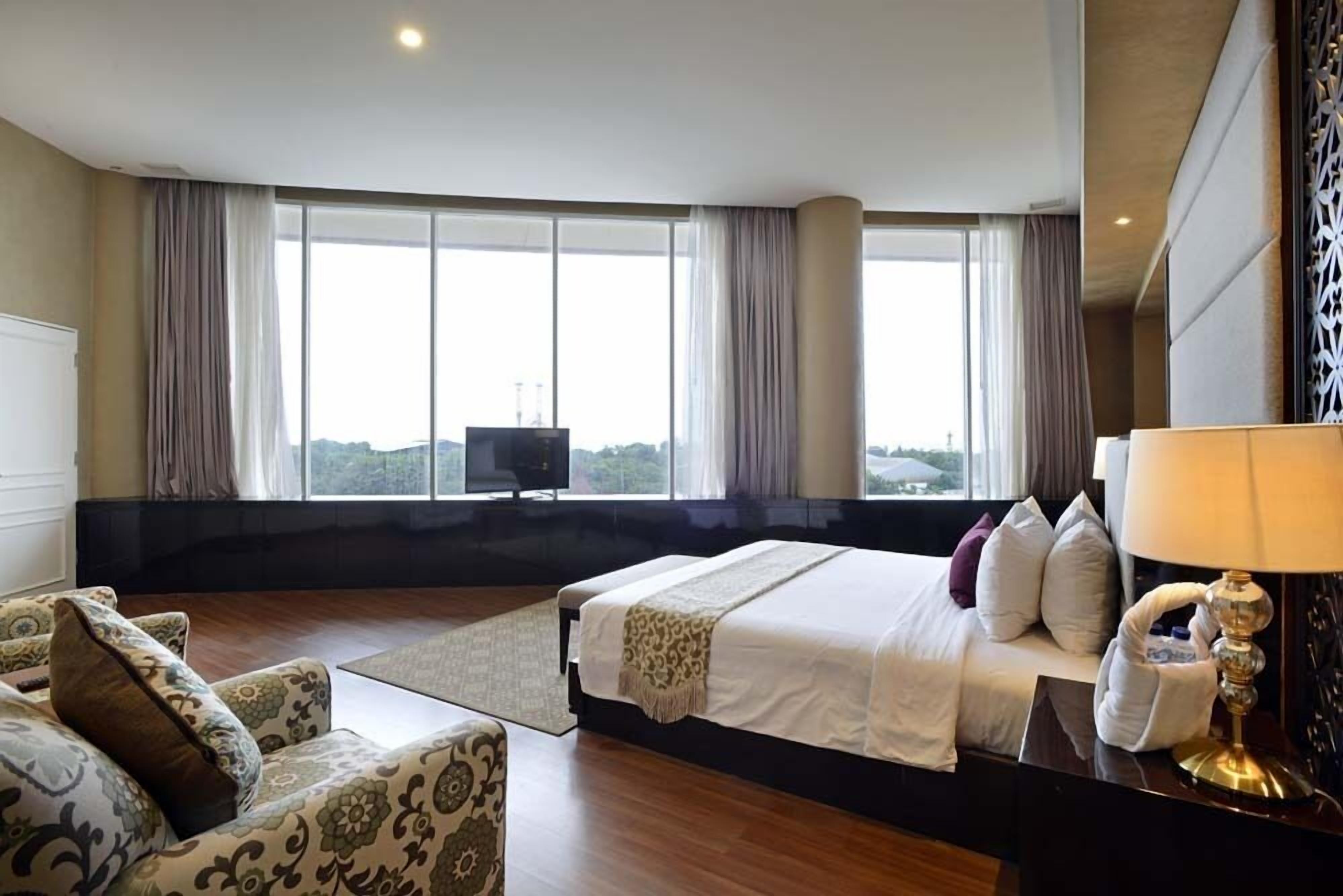 Ein Hotelzimmer mit einem großen Bett, einer Sitzecke, einem Fernseher und Blick auf die Stadt durch große Fenster.