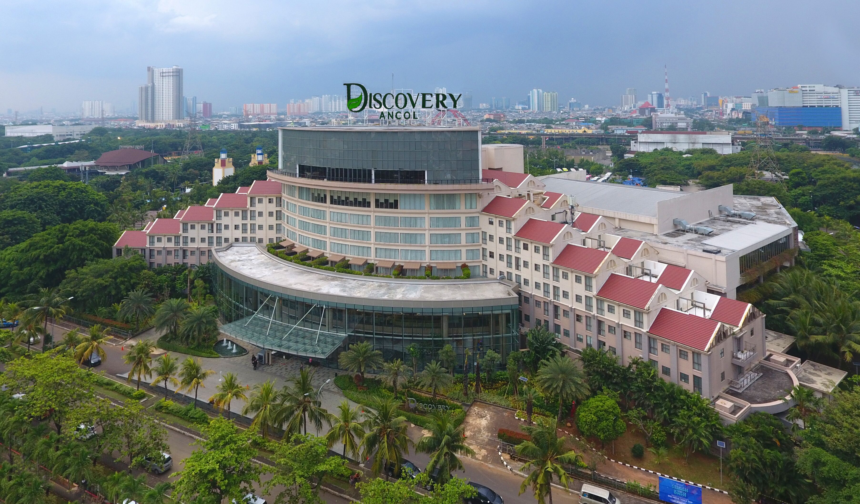 A multi-story hotel with a curved glass facade, surrounded by lush greenery and palm trees.