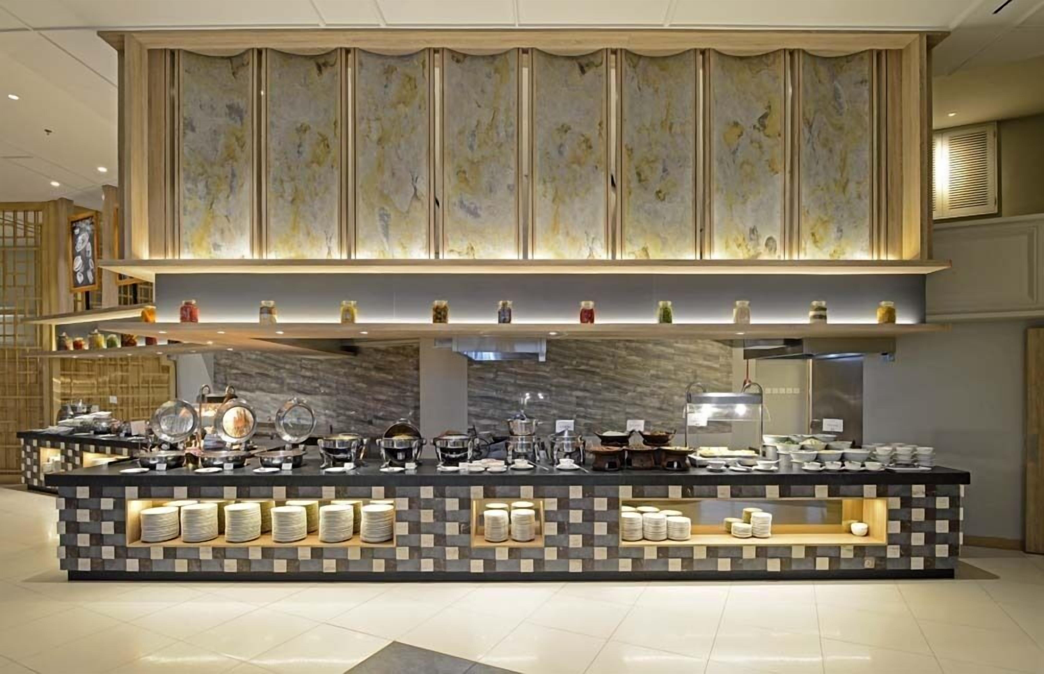 A buffet setup with a variety of dishes and utensils, a decorative wall with a floral pattern, and a tiled floor.