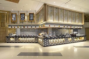 Buffet montado com várias estações de serviço, diversos recipientes de comida e uma parede decorativa com cardápio em lousa.