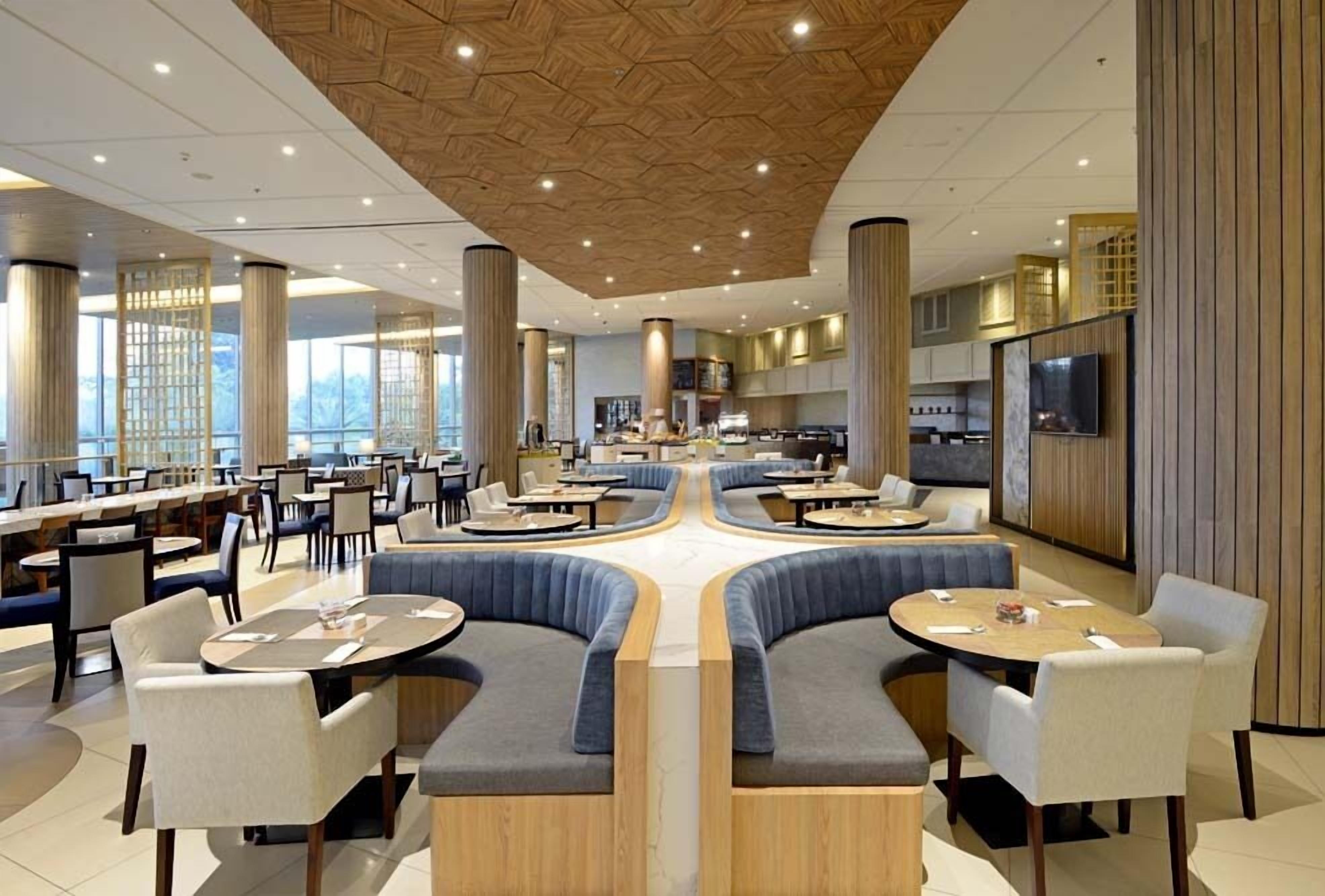 A modern restaurant with round tables, cushioned seating, and a central lounge area.