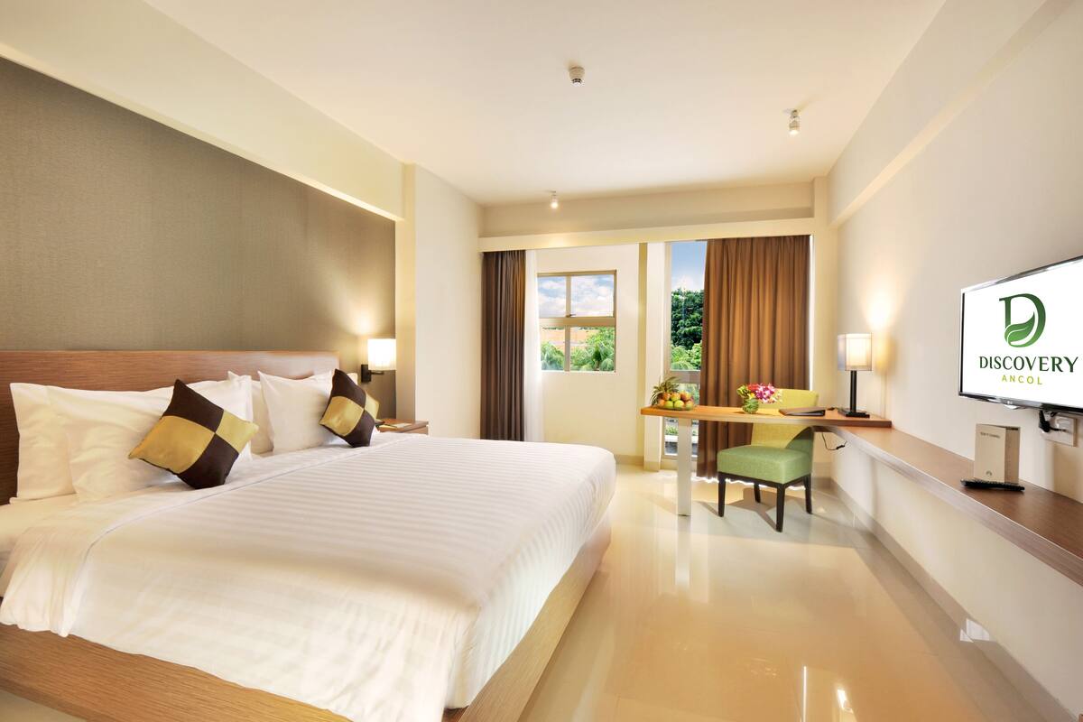 Une chambre d’hôtel avec un grand lit, un bureau avec une chaise, une télévision et une fenêtre avec des rideaux.