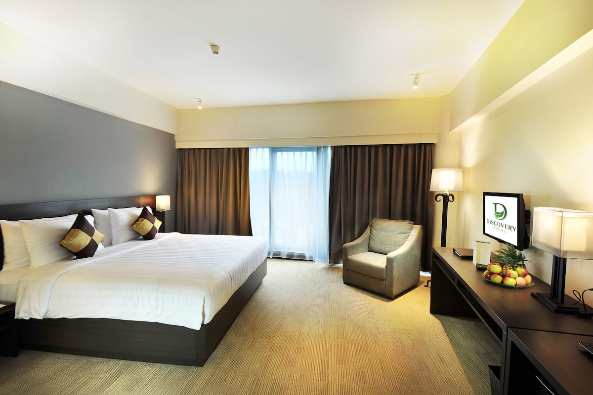 Une chambre d’hôtel avec un grand lit, une chaise, un bureau avec un ordinateur et une fenêtre avec des rideaux.