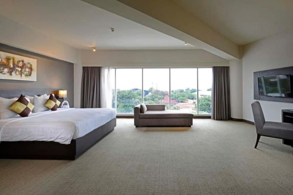 A hotel room with a large bed, a sofa, a desk, and a TV.