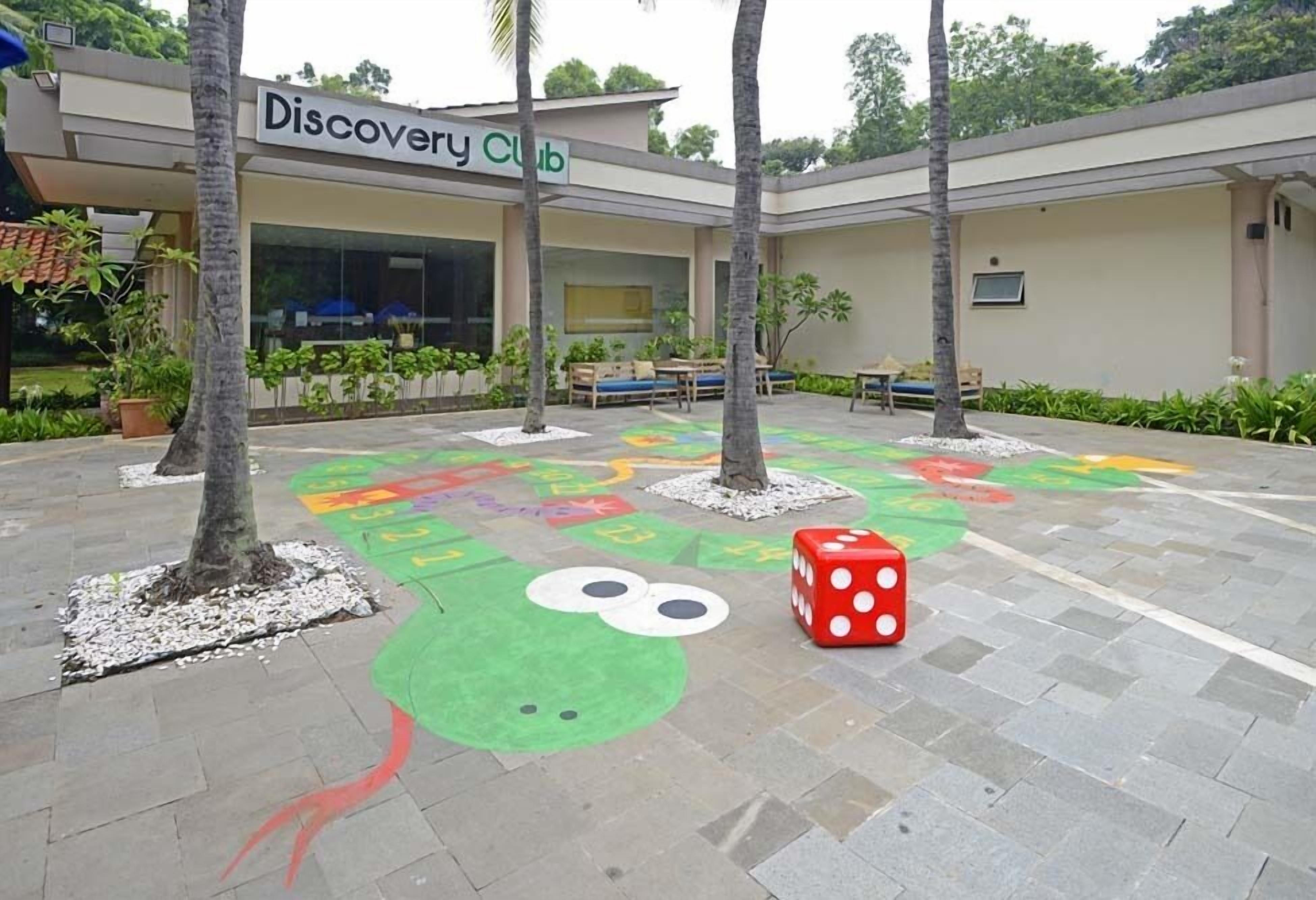 Edificio de Discovery Club con asientos al aire libre y un área de juegos colorida para niños.