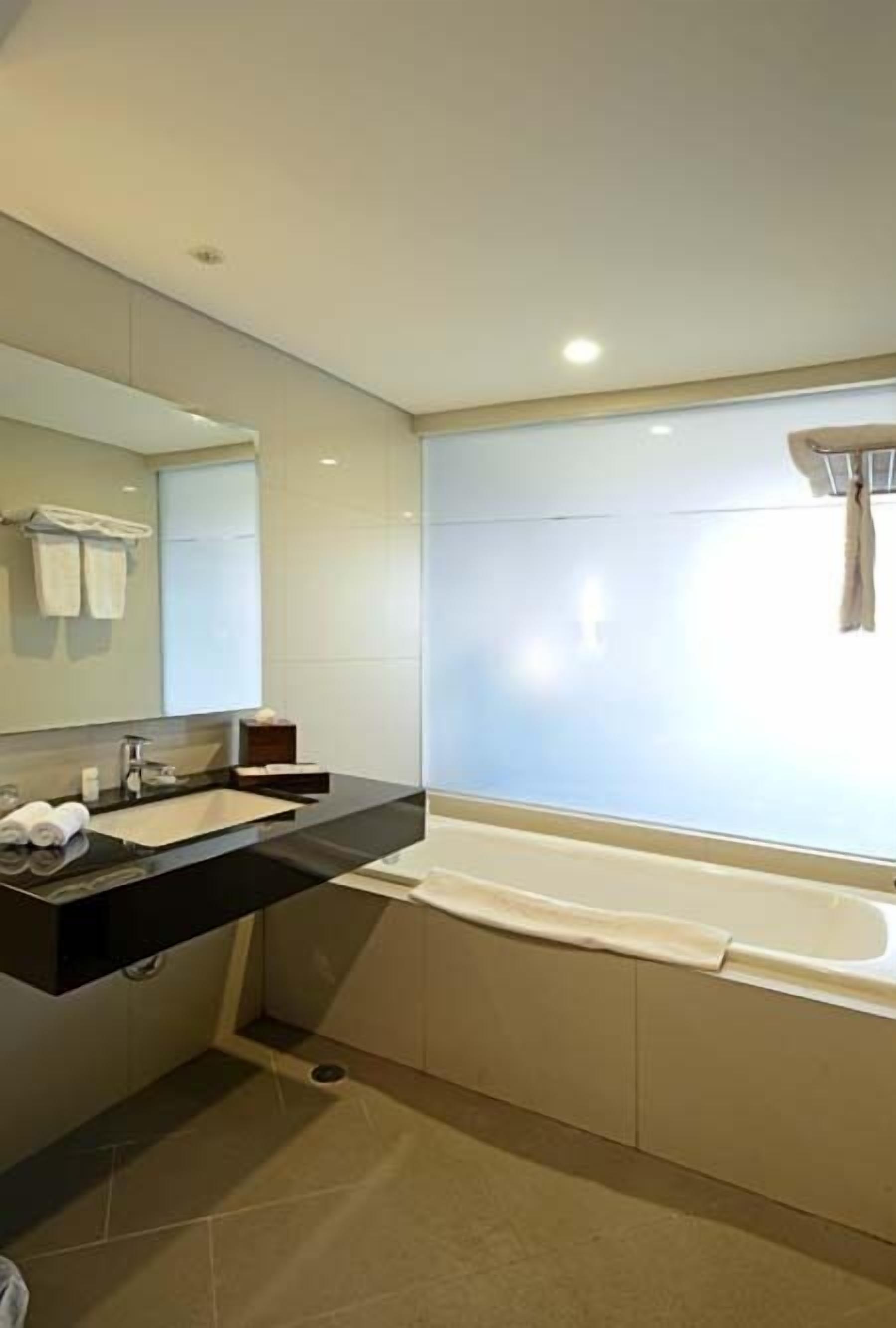A modern bathroom with a large bathtub, a vanity with a mirror, and a window with a curtain.