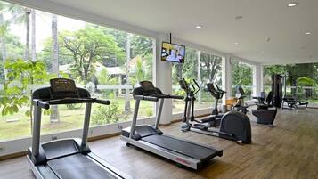A gym with treadmills, elliptical machines, and a TV screen.