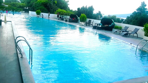 A swimming pool with a clear blue water surface, surrounded by lounge chairs and potted plants.
