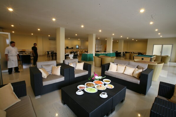 Un amplio salón con mobiliario de mimbre, mesa de billar y mesa de buffet con diversos platos.