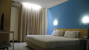 A hotel room with a bed, a desk, a chair, a telephone, and a wall-mounted light fixture.