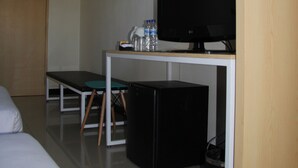 A hotel room with a bed, a desk with a television, a trash bin, and a water dispenser.