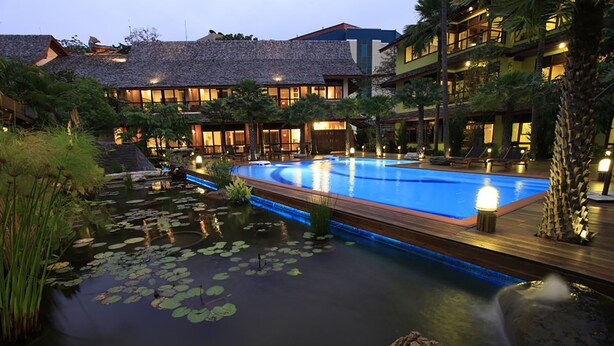 A resort with a large swimming pool surrounded by a natural landscape, including a pond with lily pads and a waterfall.