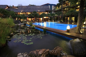 A resort with a large swimming pool surrounded by a natural landscape, including a pond with lily pads and a waterfall.