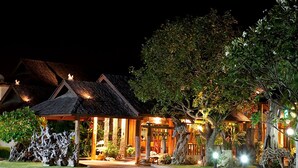A traditional-style building with a covered entrance, surrounded by lush greenery and decorative plants.