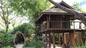 A wooden structure with a balcony, surrounded by lush greenery and a stone archway.