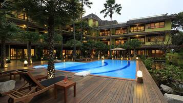 A multi-story hotel with a swimming pool surrounded by wooden deck chairs and lounge areas.