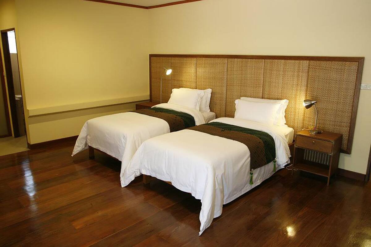 Une chambre d’hôtel avec deux lits, un plancher en bois, une tête de lit en osier et des lampes de chevet.