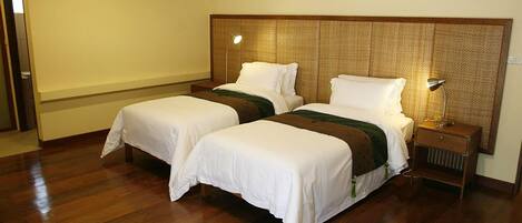 A hotel room with two beds, wooden flooring, a woven headboard, and bedside lamps.