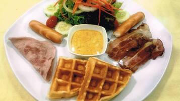 A plate with a variety of foods including a salad, sausages, a piece of meat, a waffle, and a small bowl of sauce.