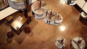 A spacious lobby with a high ceiling, featuring a central seating area with a table and chairs, surrounded by multiple hanging spherical chandeliers.
