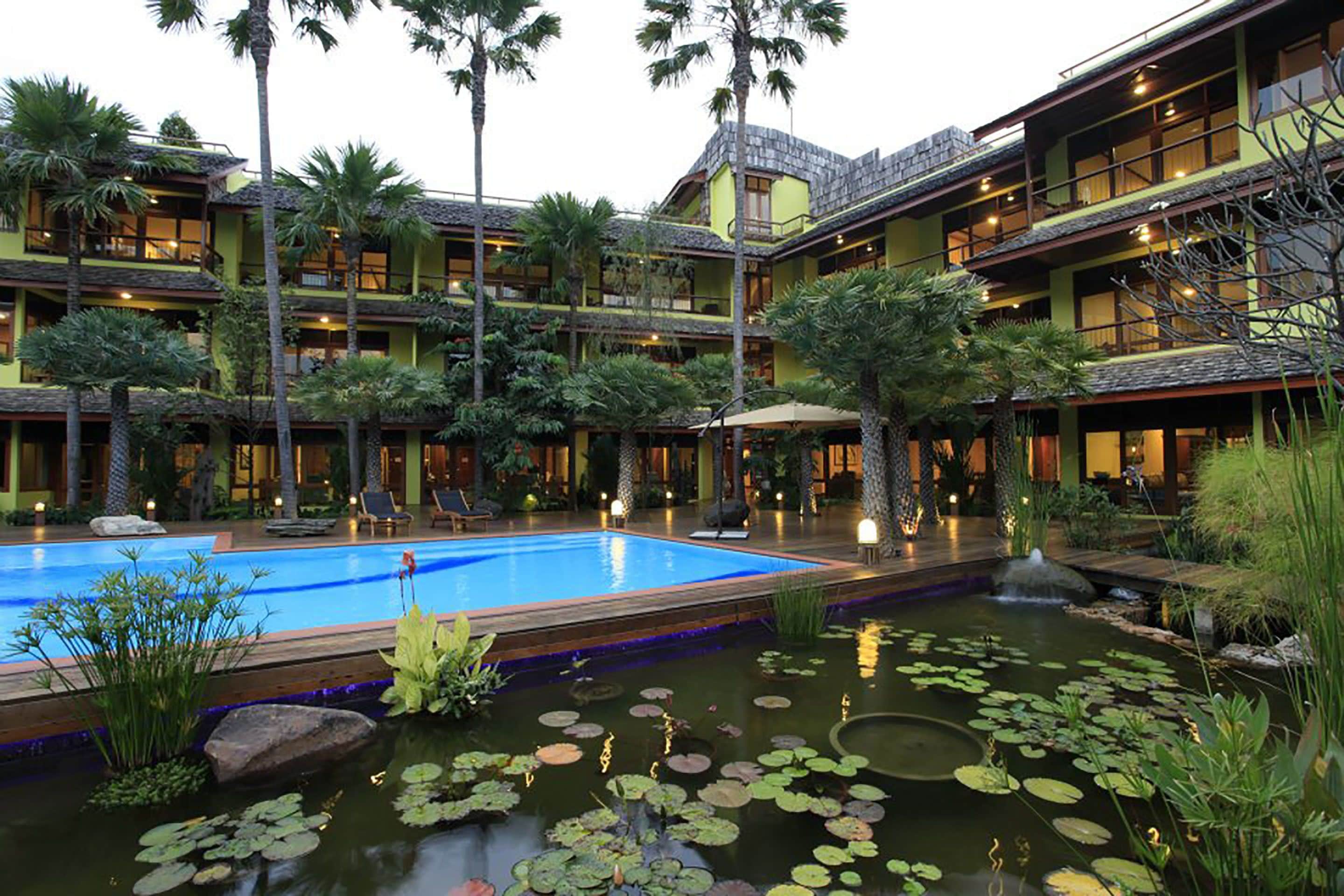 Een meerlaags hotel met een centrale binnenplaats, inclusief een zwembad en een vijver met waterlelies.